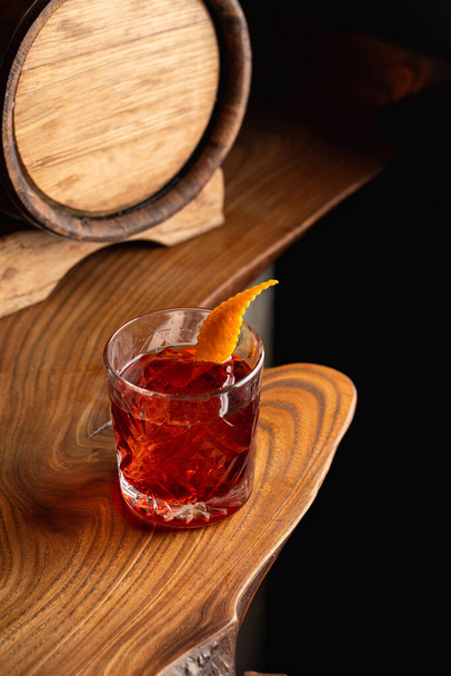 American old fashioned cocktail garnished with an orange zest, wooden barrel on a background, unusual creative wooden table - Foto, immagini