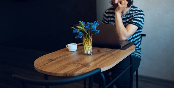 Bouquet of violets and coffee cup on wooden table against man who working at laptop. - Photo, image