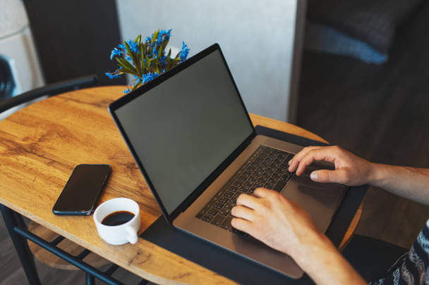 Gros plan des mains masculines tapant sur le clavier d'un ordinateur portable moderne ; homme travaillant sur un ordinateur portable ; smartphone et tasse à café sur une table en bois. - Photo, image
