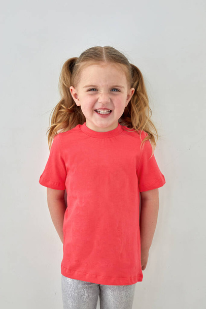 gelukkig klein meisje in roze shirt staan in studio - Foto, afbeelding