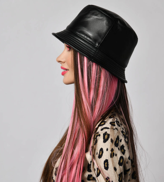 Perfil retrato de mujer hermosa sonriente con hebras de color rosa y maquillaje brillante en sombrero de cuero negro y chaqueta de leopardo - Foto, imagen