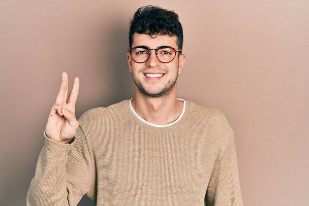 Молодой латиноамериканец в повседневной одежде и очках показывает и показывает пальцами номер три, улыбаясь уверенно и счастливо.  - Фото, изображение