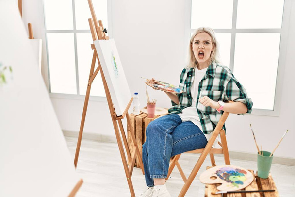 Giovane artista donna pittura su tela a studio d'arte arrabbiato e pazzo urlando frustrato e furioso, gridando con rabbia. rabbia e concetto aggressivo.  - Foto, immagini