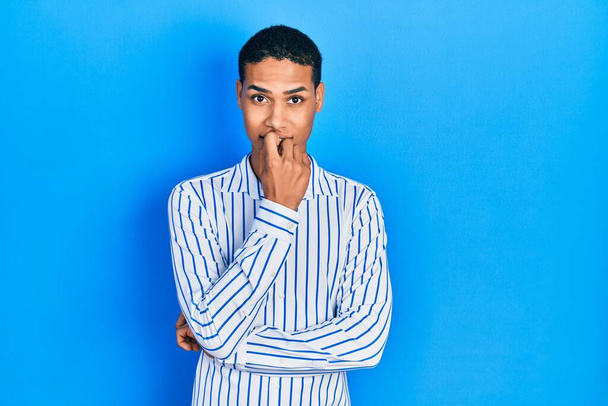 Junger afrikanisch-amerikanischer Typ in lässiger Kleidung, der gestresst und nervös aussieht und die Hände auf den Mund beißenden Nägeln hat. Angstproblem.  - Foto, Bild
