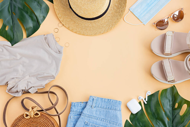 Summer composition with female fashion outfit. Monstera leaves, straw hat, bamboo bag, shoes, wireless headphones on pastel background. Flat lay, top view, overhead, mockup, template, copy space - Foto, Bild