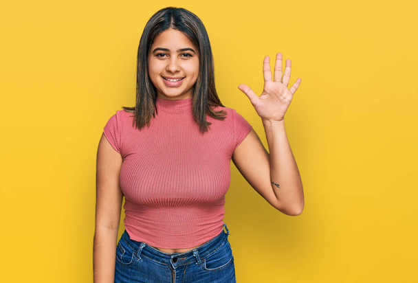 Jeune fille hispanique portant t-shirt décontracté montrant et pointant vers le haut avec les doigts numéro cinq tout en souriant confiant et heureux.  - Photo, image