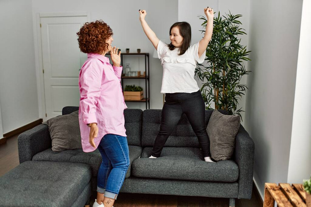 Mature mother and down syndrome daughter at home dancing on the sofa - Foto, afbeelding