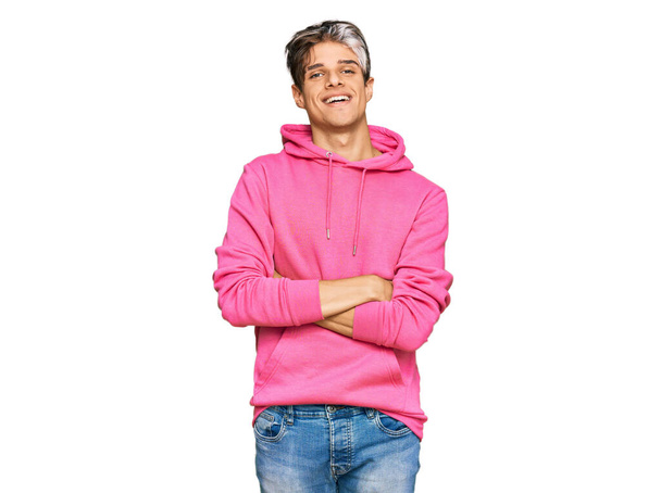 Junger hispanischer Mann in lässigem rosafarbenem Sweatshirt mit glücklichem Gesicht und verschränkten Armen, der in die Kamera blickt. positive person.  - Foto, Bild