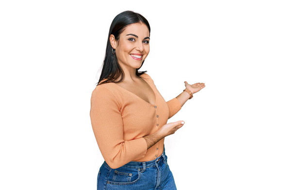 Young hispanic woman wearing casual clothes inviting to enter smiling natural with open hand  - 写真・画像