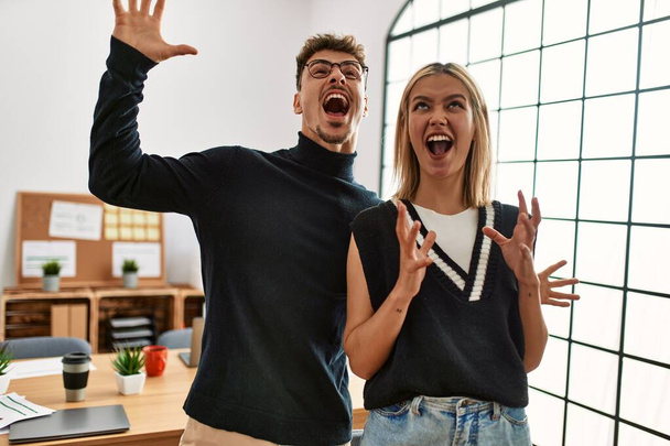 Two beautiful business workers wearing business style standing at the office crazy and mad shouting and yelling with aggressive expression and arms raised. frustration concept.  - Photo, Image