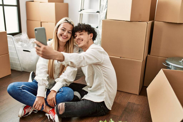 Młoda piękna para uśmiechnięta szczęśliwy make selfie przez smartfona w nowym domu. - Zdjęcie, obraz