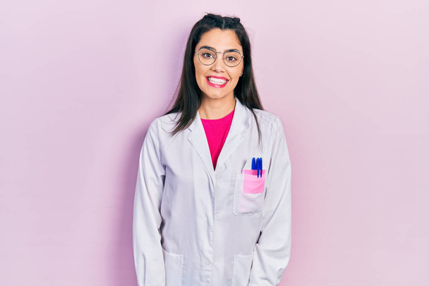 Young hispanic girl wearing scientist uniform looking positive and happy standing and smiling with a confident smile showing teeth  - Foto, immagini