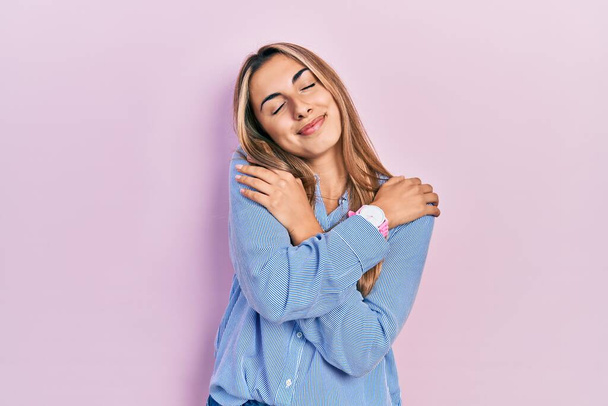 Mooie Latijns-Amerikaanse vrouw draagt casual shirt knuffelen zichzelf gelukkig en positief, glimlachend zelfverzekerd. zelfliefde en zelfzorg  - Foto, afbeelding