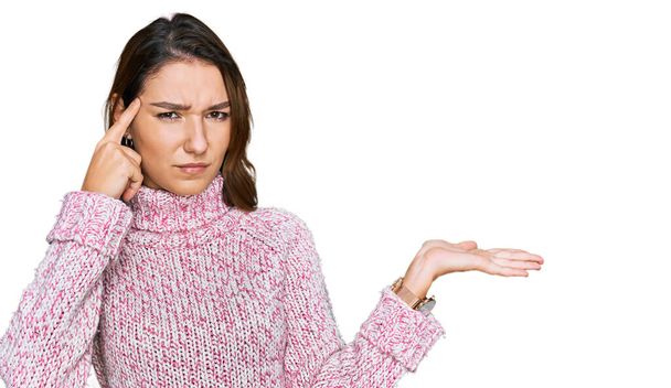 Menina caucasiana jovem vestindo suéter de lã inverno confuso e irritado com a palma aberta mostrando espaço de cópia e apontando o dedo para a testa. Pense nisso..  - Foto, Imagem