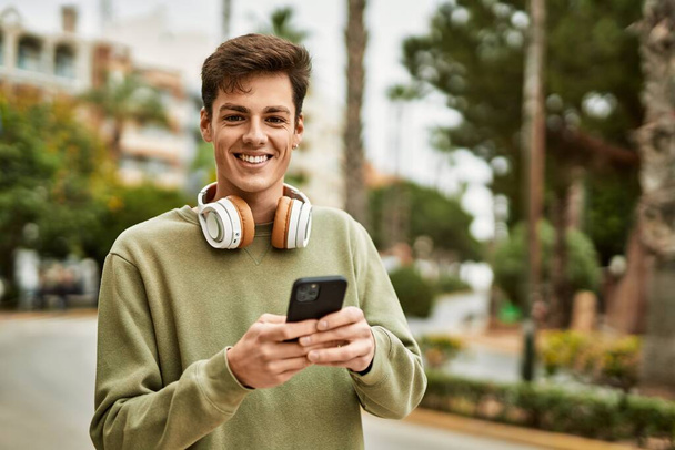 Genç İspanyol adam şehirde akıllı telefon ve kulaklık kullanarak mutlu gülümsüyor.. - Fotoğraf, Görsel