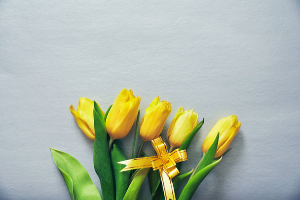 Pięć żółtych tulipanów na szarym tle z żółtą wstążką i przestrzenią do kopiowania - Zdjęcie, obraz