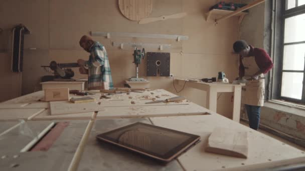 Medium shot van blanke en Afro-Amerikaanse ambachtslieden die met hout werken in schrijnwerkplaats - Video