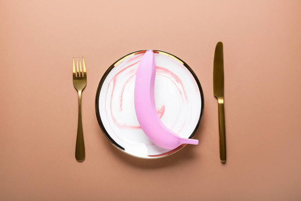 Composition with table setting and painted banana on color background - Photo, Image