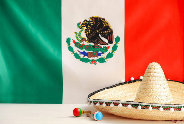 メキシコの旗に対するテーブルの上のソムブレロ帽子とマラカス - 写真・画像