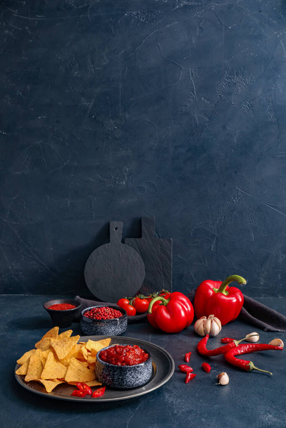 Composição com molho de pimenta saboroso, ingredientes e nachos no fundo escuro - Foto, Imagem