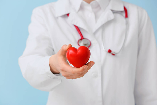 Doctor with red heart on color background, closeup - Foto, Bild