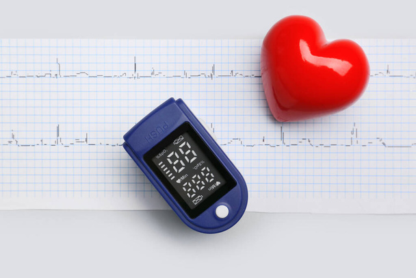 Κόκκινη καρδιά με παλμικό οξύμετρο και καρδιογράφημα σε γκρι φόντο - Φωτογραφία, εικόνα