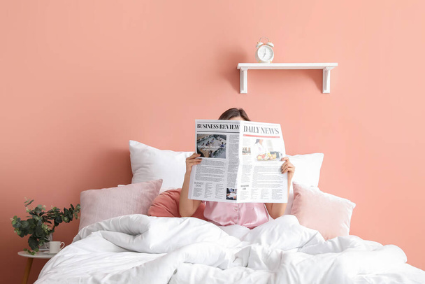 Young woman reading newspaper in bedroom - 写真・画像