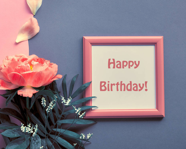 Happy birthday card with peony flower and petals. Single flower and white frame on pink and dark grey layered grey paper background. Creative flat lay with floral decor. Greeting card design. - Фото, изображение