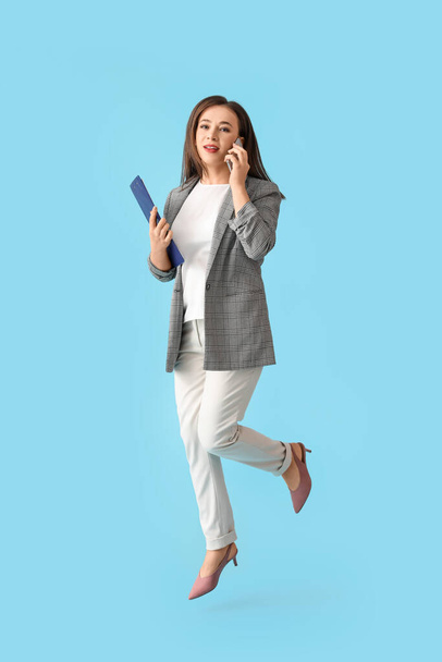 Jumping young woman talking by mobile phone on color background - Foto, immagini