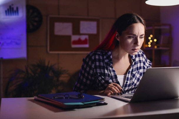 Beautiful woman working with laptop in office at night - Фото, зображення