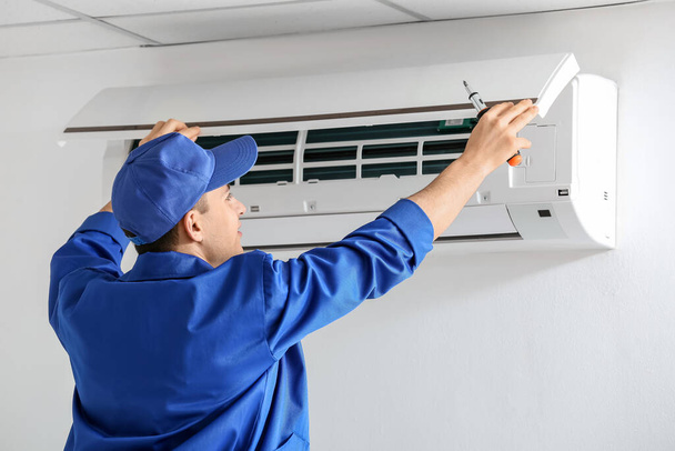 Junger Elektriker repariert Klimaanlage in Innenräumen - Foto, Bild