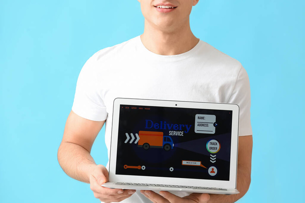 Young man and laptop with open page of delivery service application on color background - Photo, Image