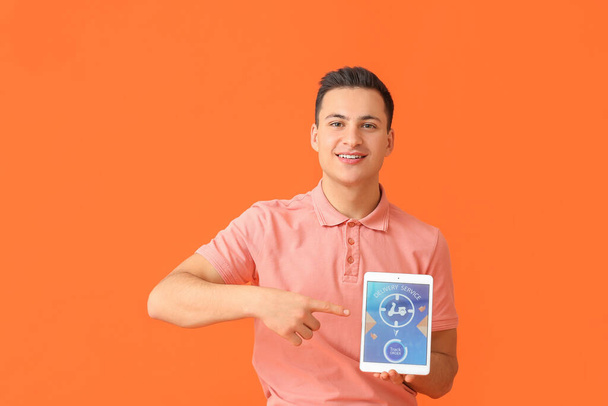 Young man and tablet computer with open page of delivery service application on color background - Fotó, kép