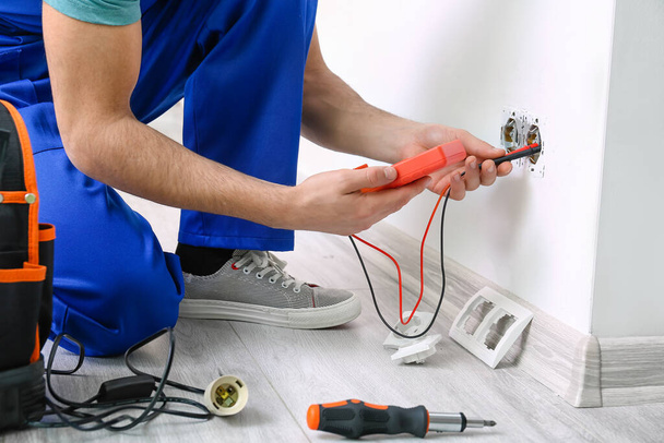 Young electrician measuring voltage of socket in room, closeup - Photo, Image