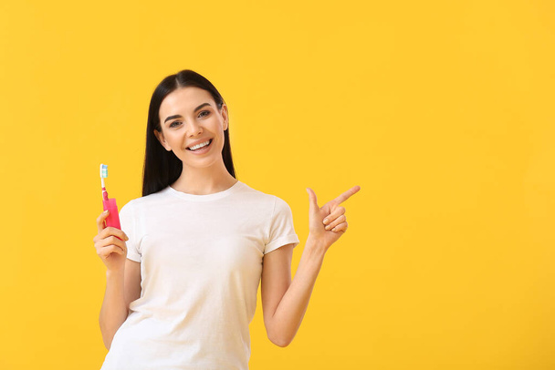 Mladá žena se zubním kartáčkem ukazuje na něco na barevném pozadí - Fotografie, Obrázek