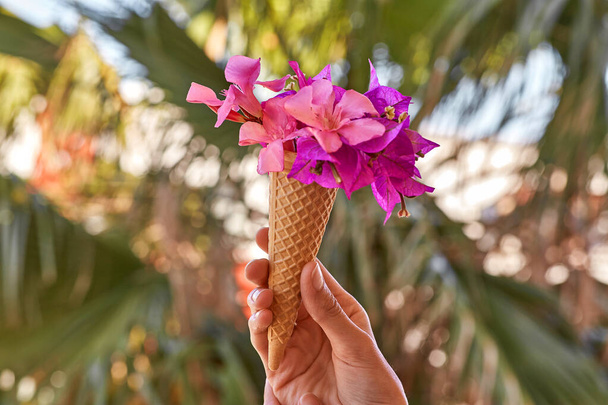A nő fényes rózsaszín virágokat tart Bougainvillea fagylaltkúpban a pálmalevelek hátterében napsütéses időben. Reklám koncepció az utazás és a fényes nyári vakáció. Nyári szürreális virágok - Fotó, kép