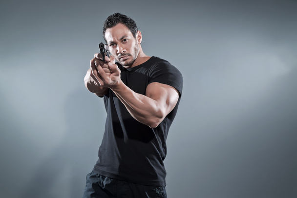 Action hero muscled man shooting with gun. Wearing black t-shirt - Foto, immagini
