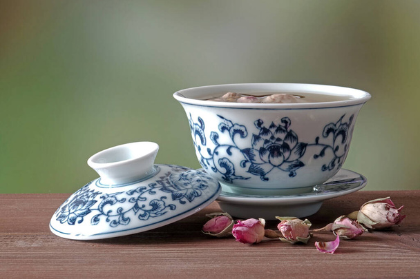 Rose Tea im traditionellen chinesischen Stil blau-weiße Poreclain Teetasse auf Holztisch, selektiver Fokus mit unscharfem naturgrünem Hintergrund. - Foto, Bild