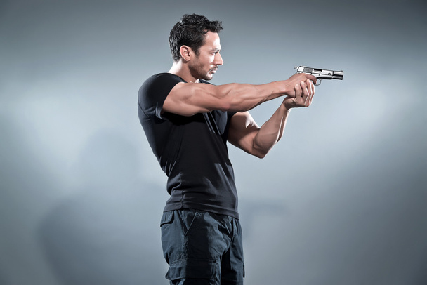 Acción héroe musculoso hombre disparando con arma. Usando camiseta negra
 - Foto, Imagen