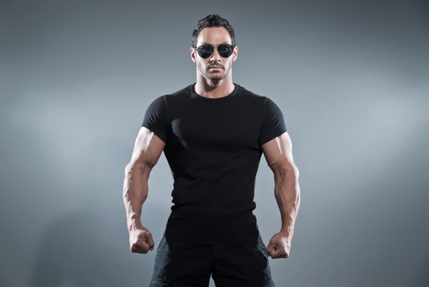 Боевой мускулистый герой боевика в черной футболке с брюками
  - Фото, изображение