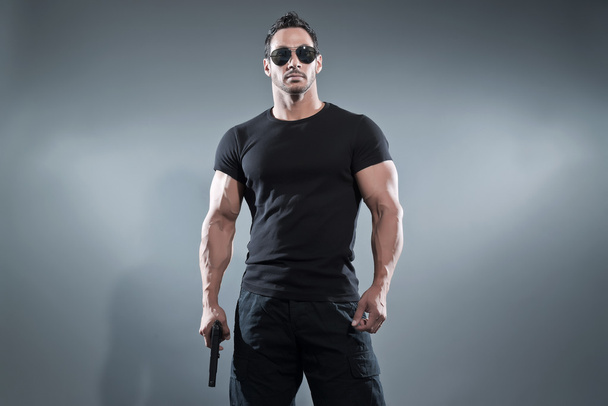 ήρωας δράσης μυώδης άνθρωπος που κρατά ένα όπλο. Φορώντας μαύρο μπλουζάκι πνεύμα - Φωτογραφία, εικόνα
