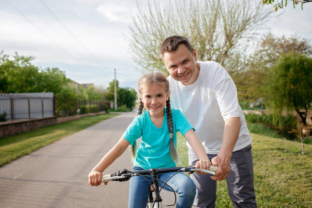 Батько навчає свою маленьку доньку їздити на велосипеді, здоровий спосіб життя в селі в літній день
 - Фото, зображення