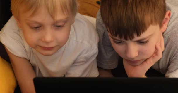 Twee jongens liggen op de bank en spelen op een laptop. Vooraanzicht. Sluiten. - Video