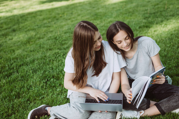 Dos alumnas están sentadas en el parque en el césped con libros y computadoras portátiles, estudiando y preparándose para los exámenes. Educación a distancia. Enfoque selectivo suave. - Foto, imagen