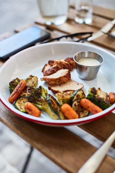 ψητό κοτόπουλο με λαχανικά με σάλτσα σε ξύλινο τραπέζι στη βεράντα ενός τοπικού εστιατορίου - Φωτογραφία, εικόνα
