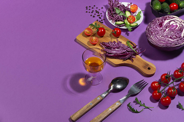 Raw healthy salad ingredients - purple cabbage, red tomatoes, cucumber, arugula in sunlight with shadow on modern violet color background, top view. - Fotó, kép