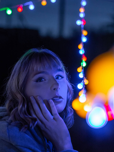 A vertical portrait of a young blonde caucasian female with colorful street lights - Foto, Imagen