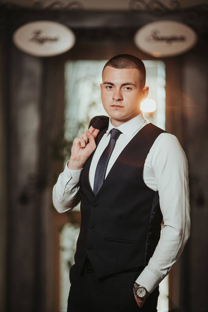 A vertical shot of a young caucasian male club manager posing holding his jacket - Fotografie, Obrázek