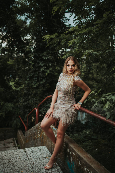 A vertical shot of a young stylish female in a cocktail dress leaning to the handrail outdoors - Fotoğraf, Görsel