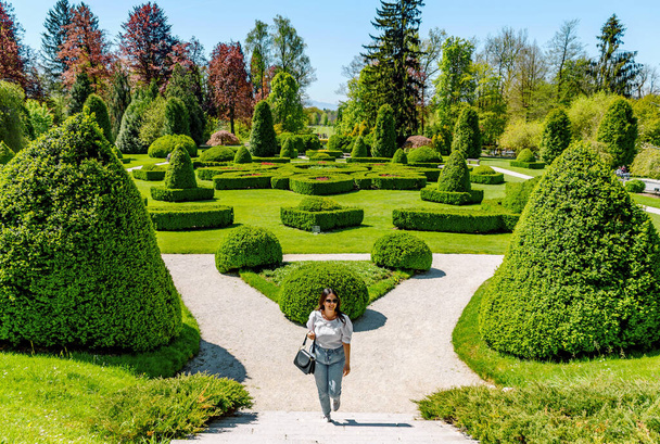 Young woman walking on path in beautiful green park with hedge shapes and trees at Arboretum volcji potok near Radomlje in Slovenia. - Zdjęcie, obraz